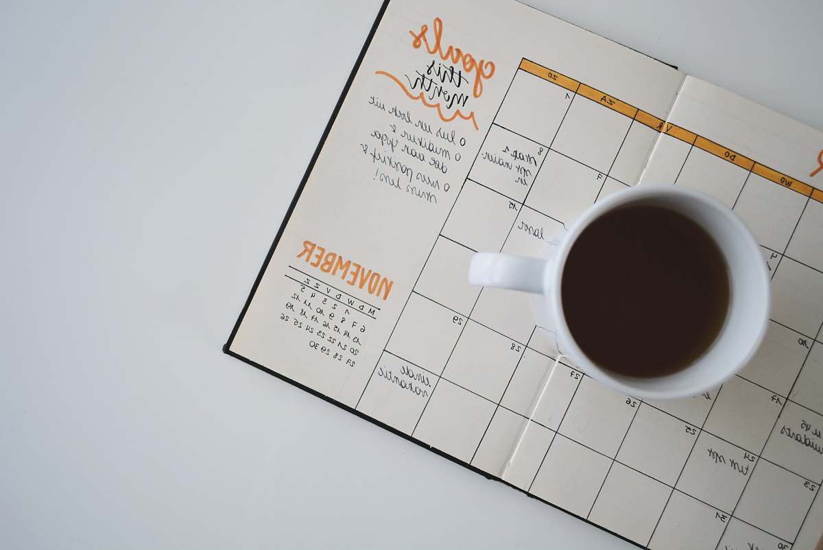 goal white ceramic mug with coffee on top of a planner journal