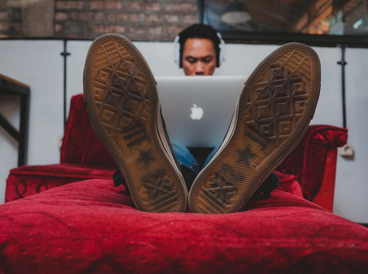 clothing man using MacBook on sofa cowboy boot