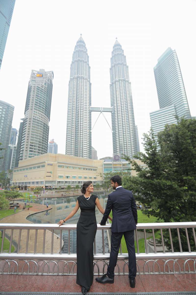 city a man and a woman in black with the Petronas tower at the background high rise