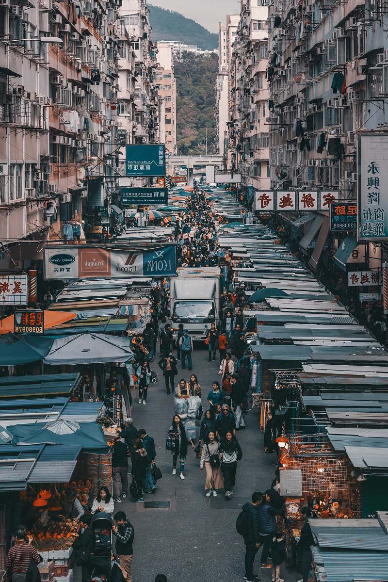 city aerial photography of people walking past display stalls between concrete buildings during daytime metropolis