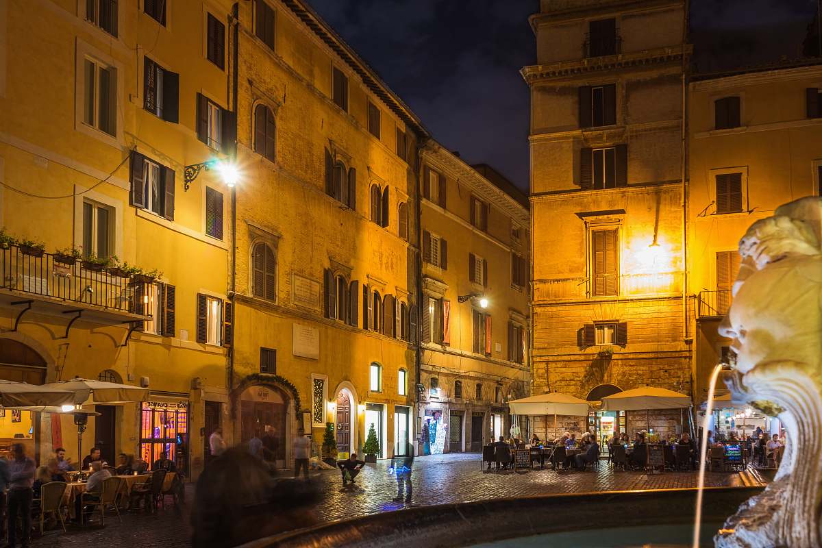 city people walking and standing near brown concrete buildings during nighttime downtown
