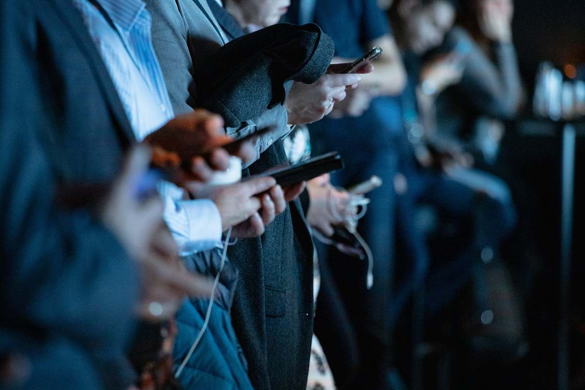 Capture the essence of modern communication with this vibrant image featuring a diverse group of people standing in a stylish office environment, each engaged with their smartphones. This scene reflects the dynamic interplay of fashion and technology, showcasing how apparel and digital connectivity interact in today's professional settings. Perfect for articles about workplace culture, technology trends, or marketing campaigns targeting millennials and Gen Z.
