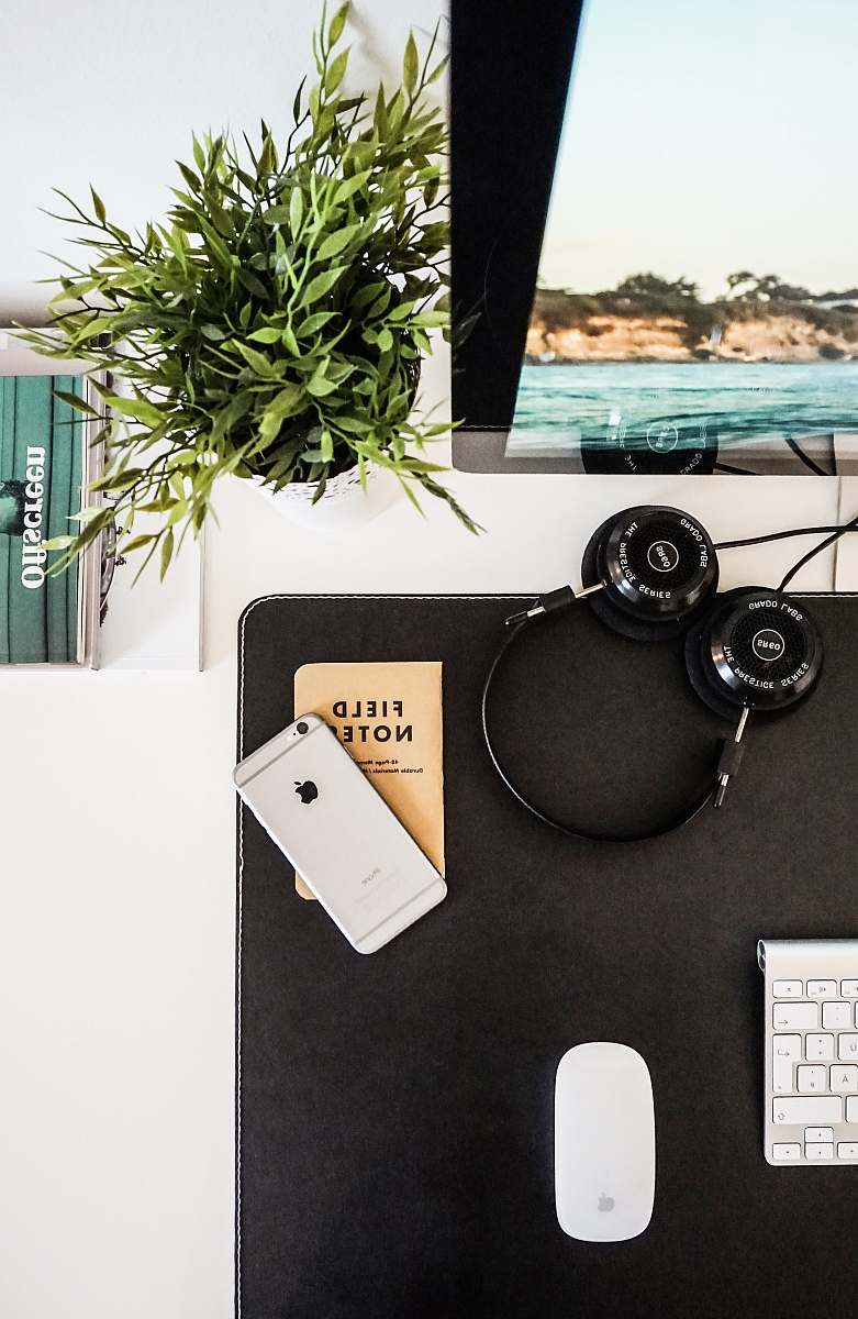 workspace black headphones beside space gray iPhone on brown table plant