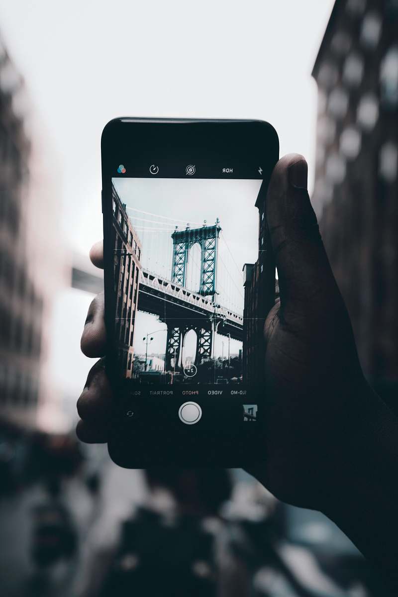phone grayscale photography of person holding iPhone capturing bridge mobile phone