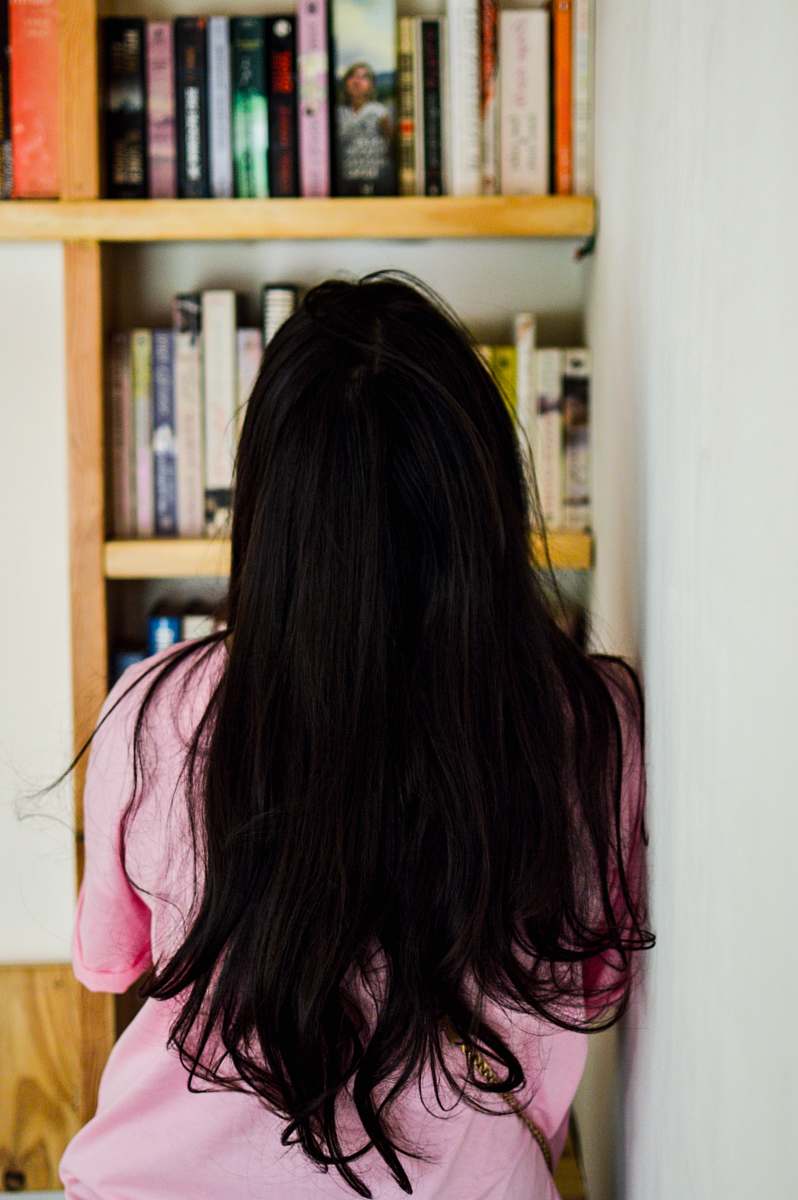 human woman leaning on wall looking at bookshelf person