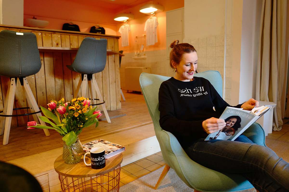 chair woman reading book while sitting on sofa chair in front of bar counter and stools person
