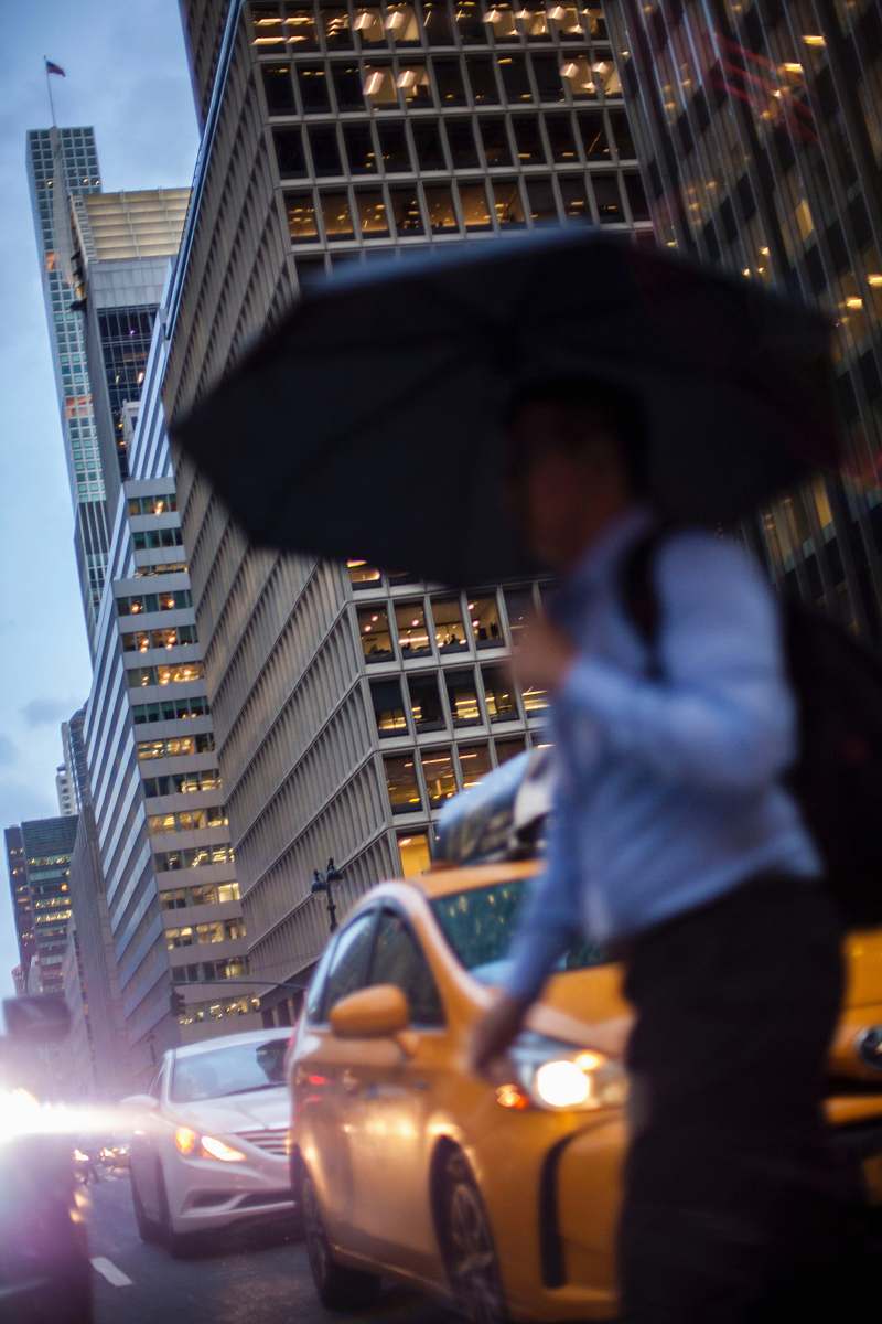 person man in blue dress shirt holding umbrella crossing street during daytime people
