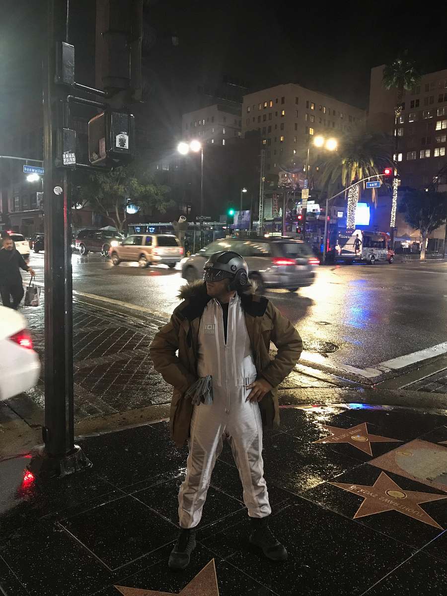 person man in white jumpsuit with brown jacket posing near road pedestrian