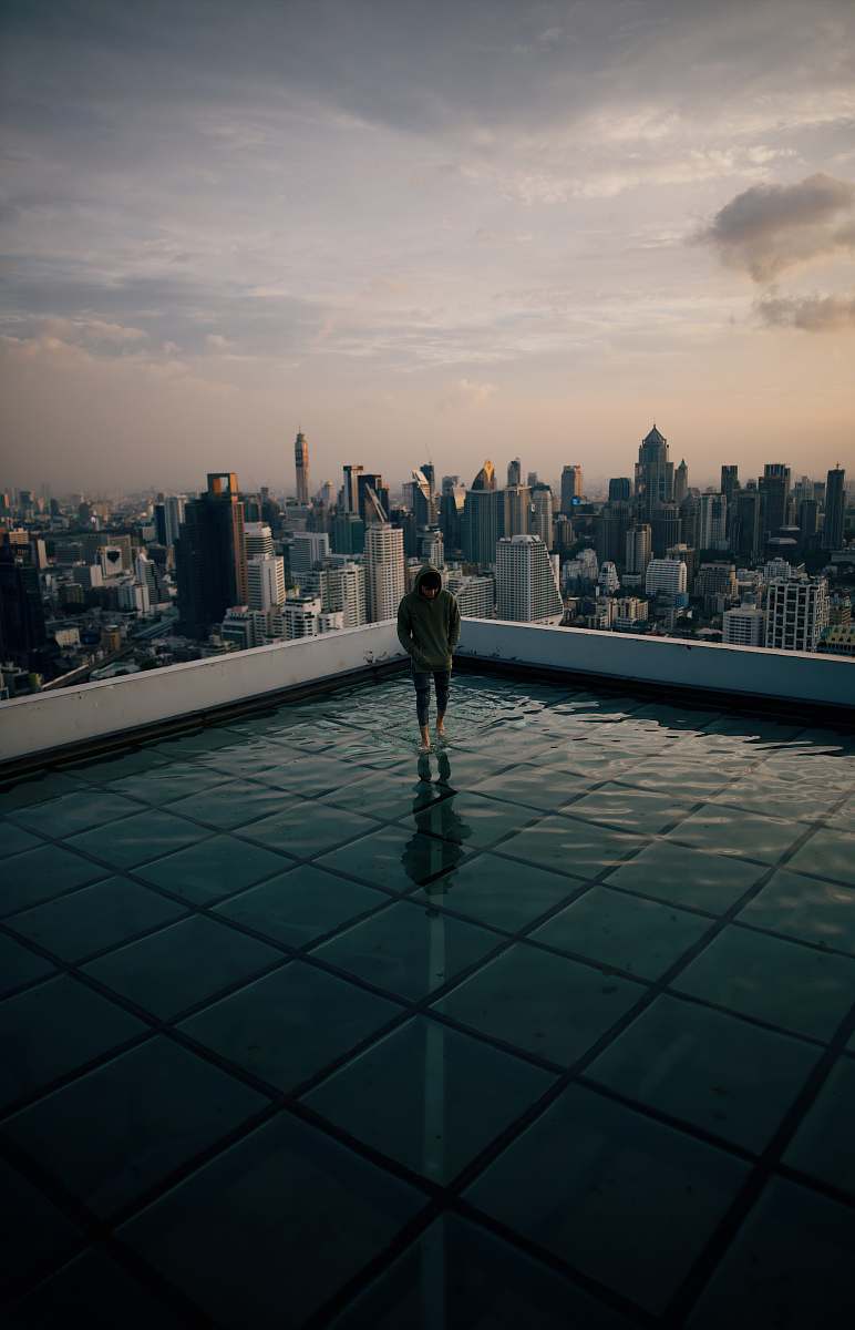 person man standing on top of building facing high-rise building under gray sky urban