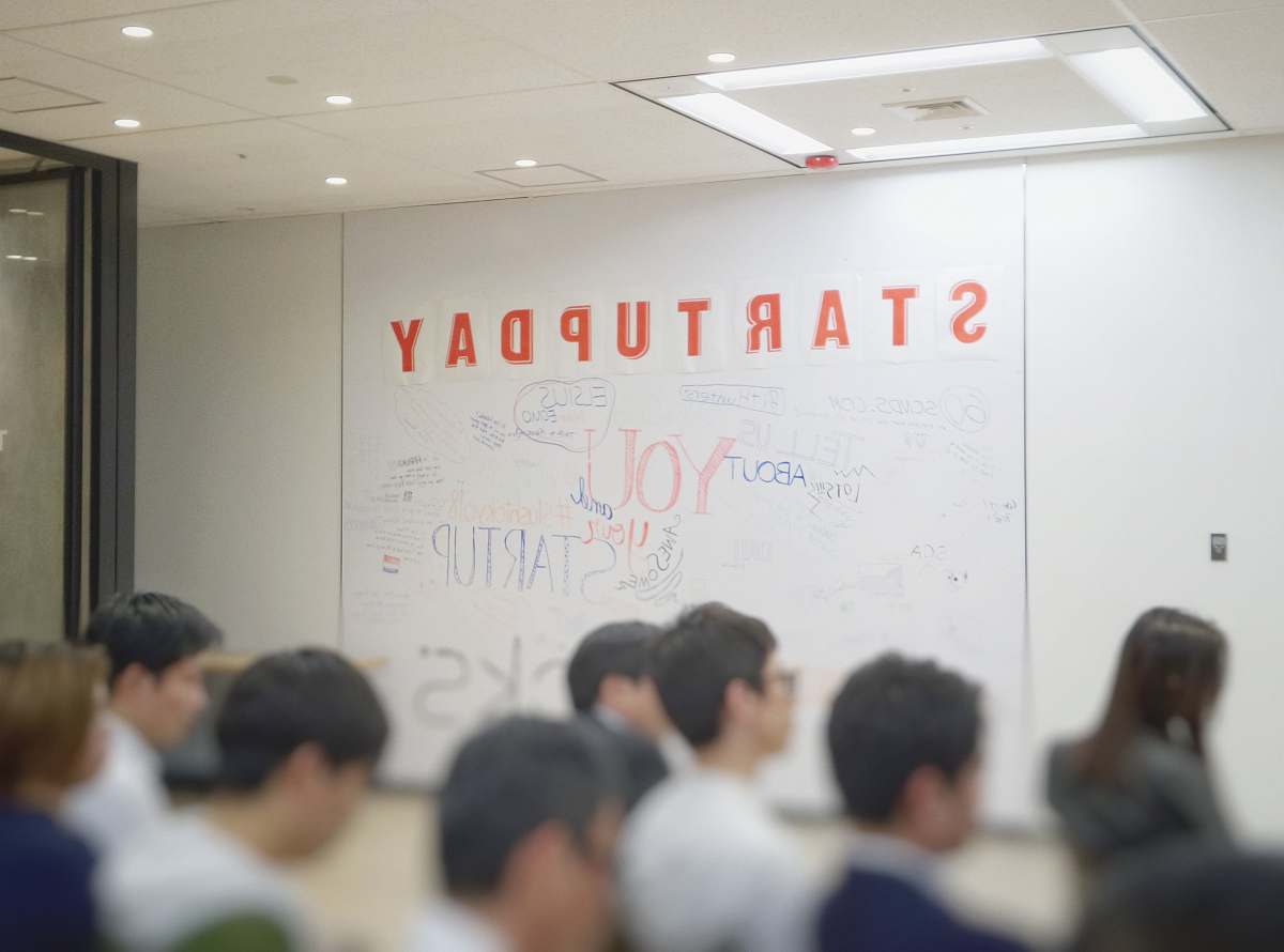 Capture the essence of innovation and teamwork at a Startup Day event, featuring a diverse group of individuals gathered in a contemporary room. A focused man stands confidently in front of a whiteboard, sharing insightful ideas and strategic messages with his peers. This image encapsulates the spirit of entrepreneurship and collaboration, making it ideal for articles, blogs, or marketing materials related to startups, business development, and team dynamics.