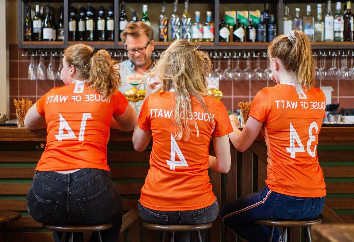person three woman wearing orange t-shirts sitting on bar stools pub