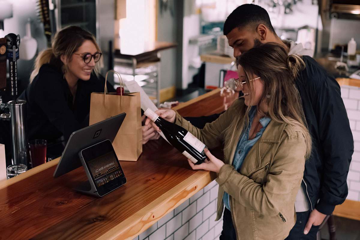 person woman holding wine bottle beside man in front of woman smiling wood