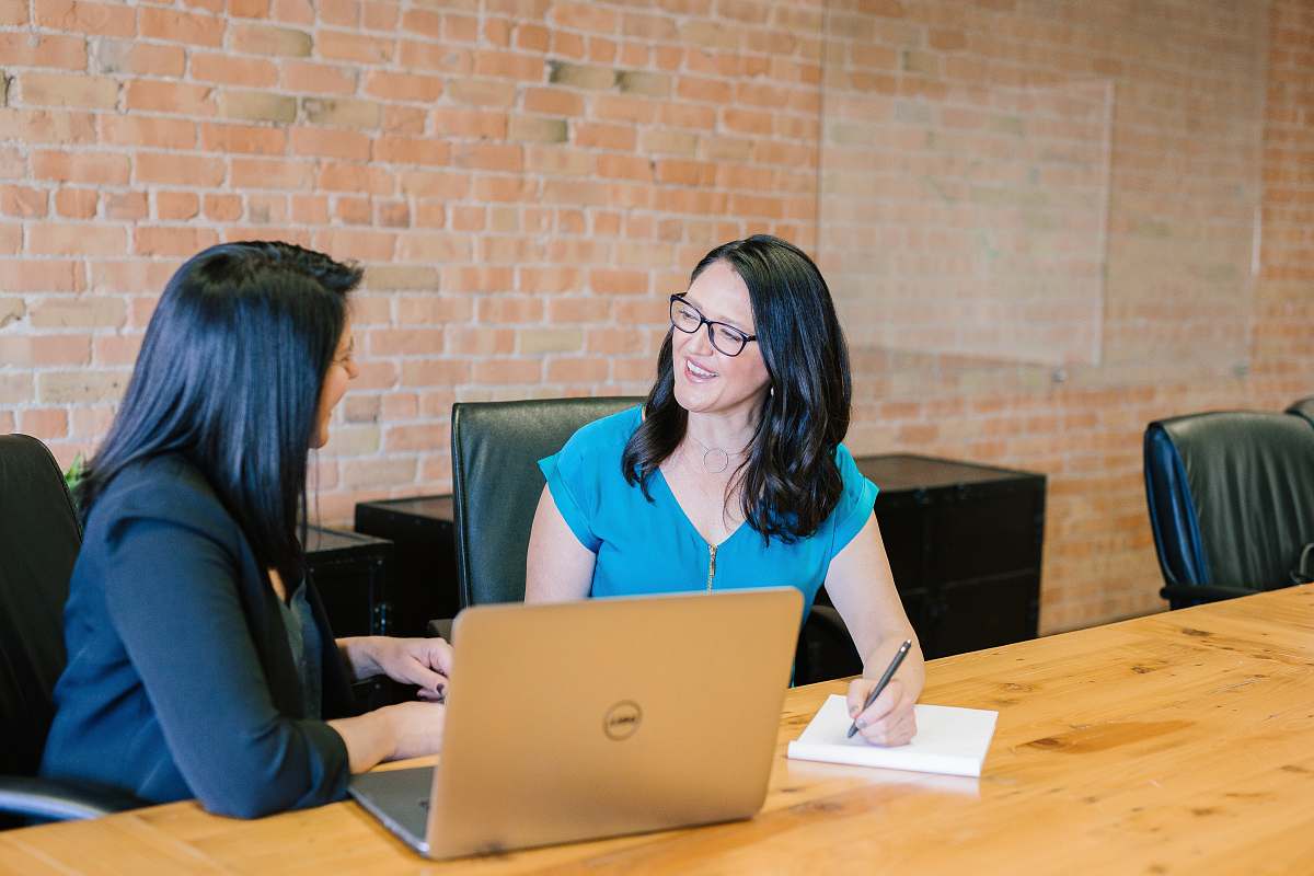 person woman in teal t-shirt sitting beside woman in suit jacket sitting