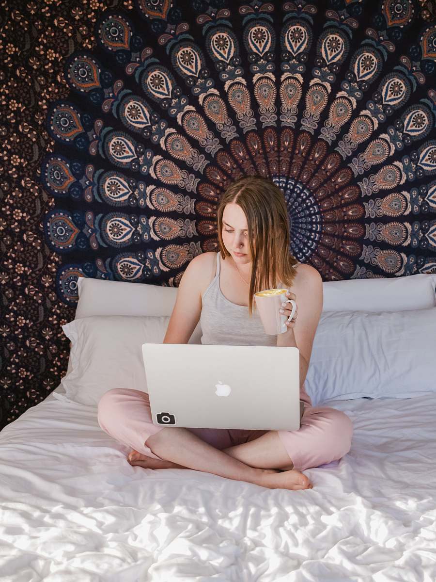 laptop woman sitting on bed using laptop while holding mug furniture