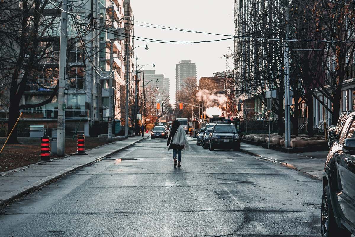 city woman walking near vehicles parked on road between large buildings road