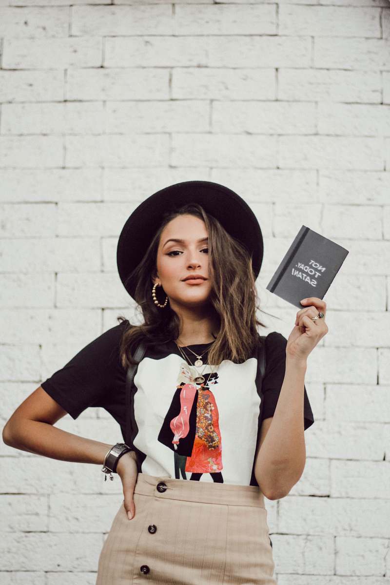 person woman with left arm akimbo standing while holding leaflet hat