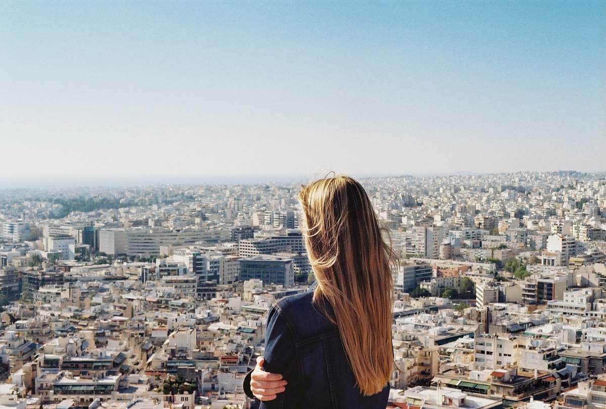 This captivating image features a woman dressed in a stylish black T-shirt, standing confidently on a ledge as she gazes over a vibrant city skyline. The scene captures a moment of reflection and wonder, making it perfect for use in lifestyle blogs, urban exploration articles, or advertisements promoting self-discovery and personal growth. With the city as her backdrop, this photo exudes a sense of freedom and adventure, ideal for creative projects that celebrate individuality and urban life.