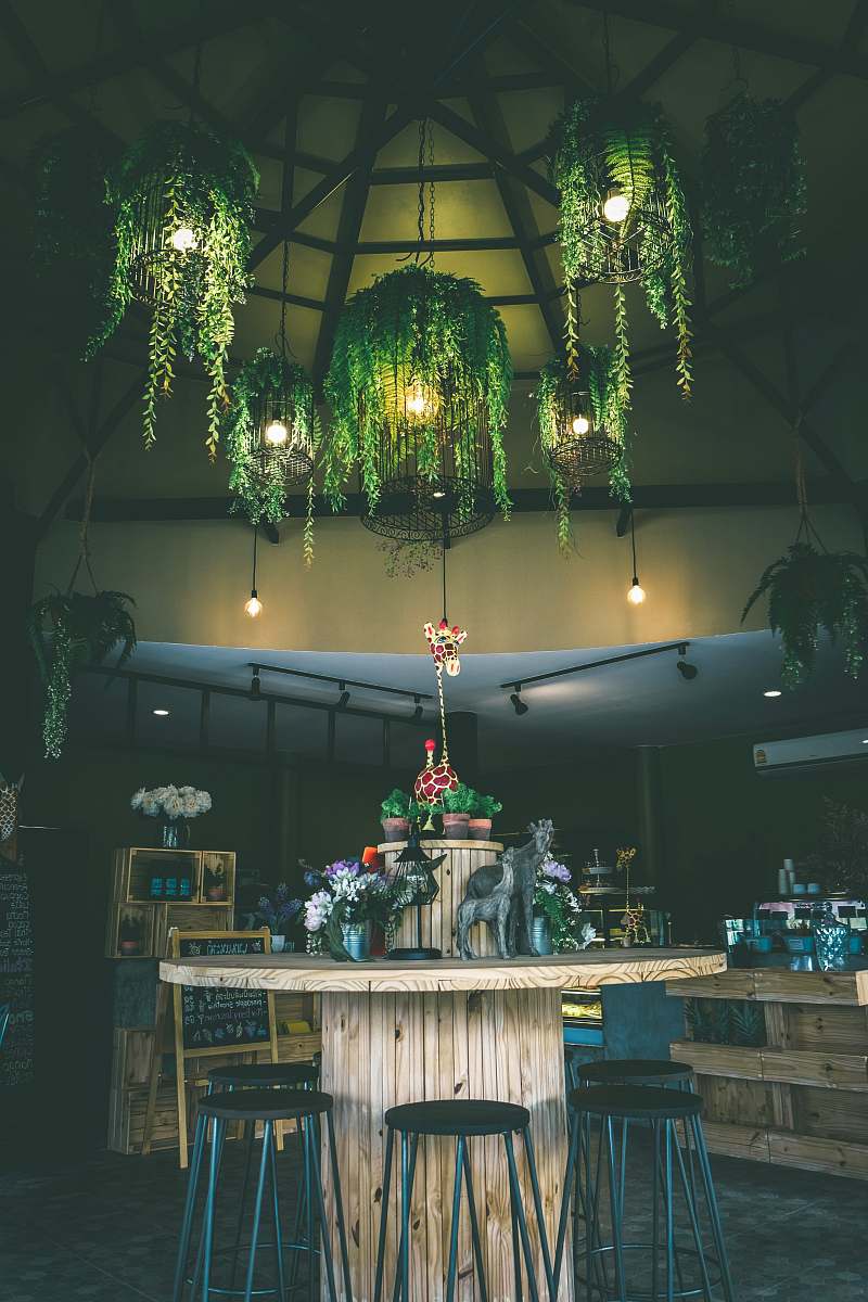 room round brown wooden table surrounded by black stools under green leafed-themed pendant lamps lighting