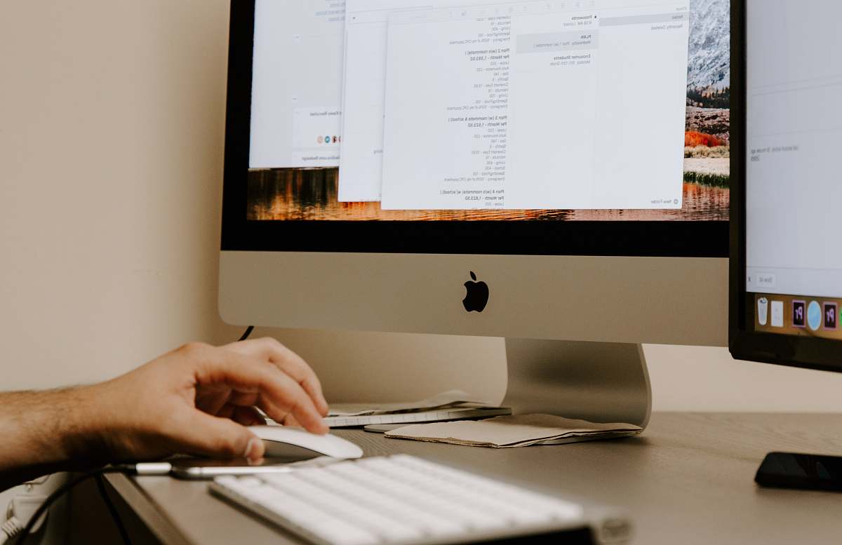 hardware person holding white Apple Magic Mouse beside iMac and keyboard electronics