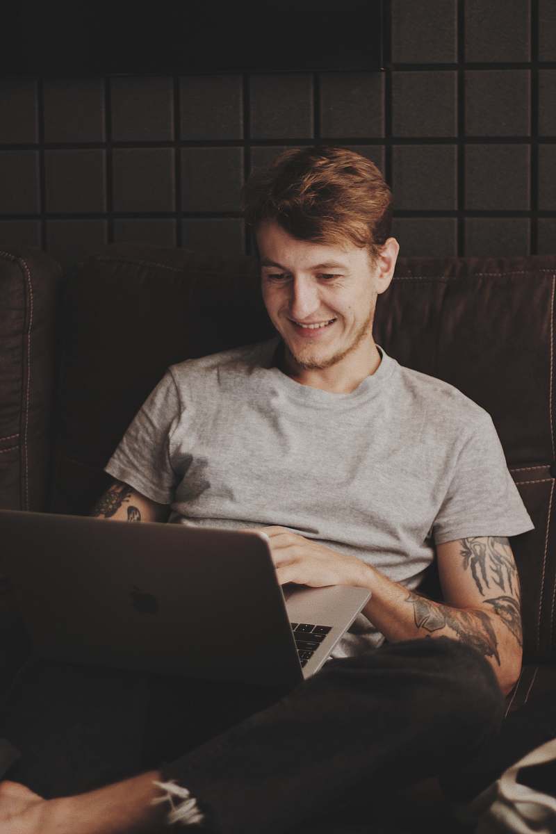 furniture man sitting facing silver MacBook inside room couch