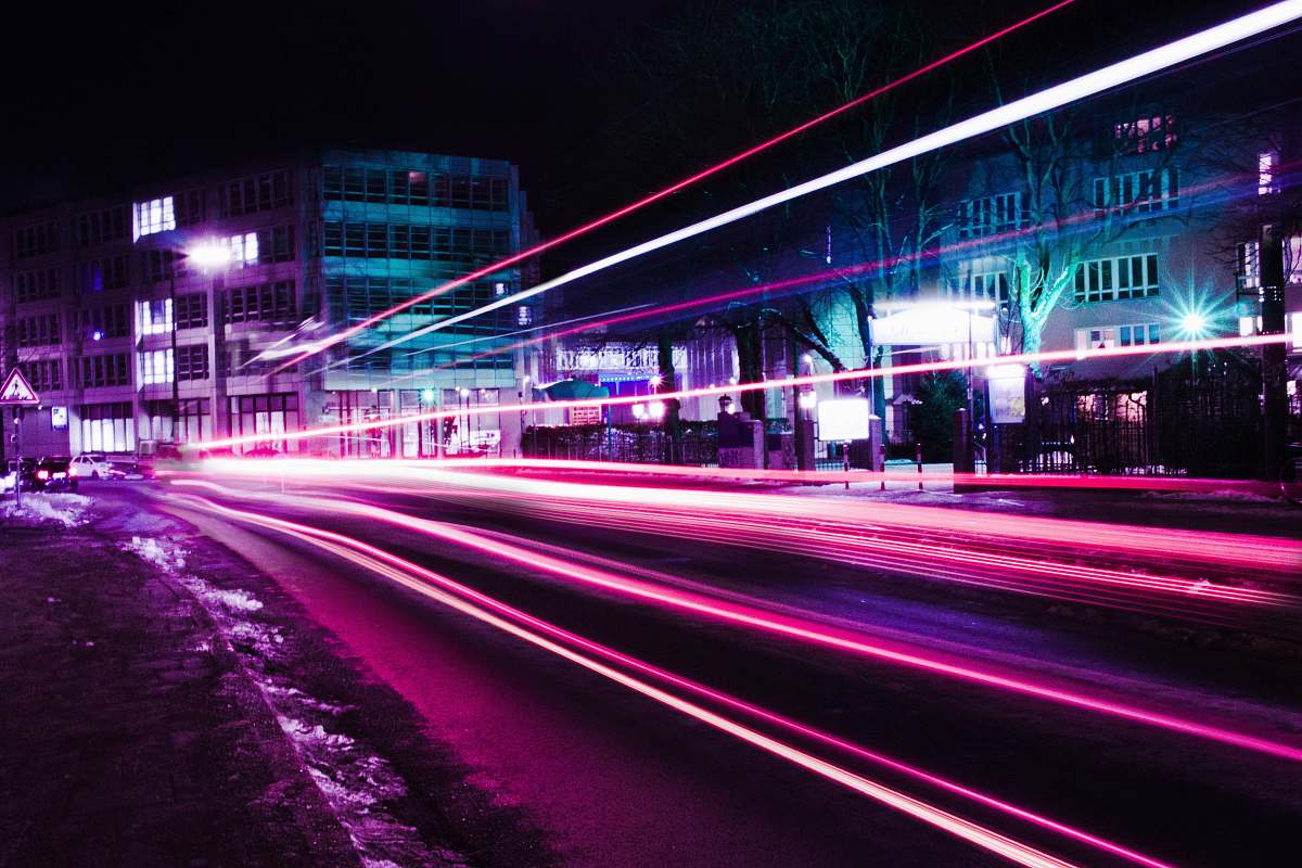 neon timelapse photography of pink vehicle lights near buildings purple
