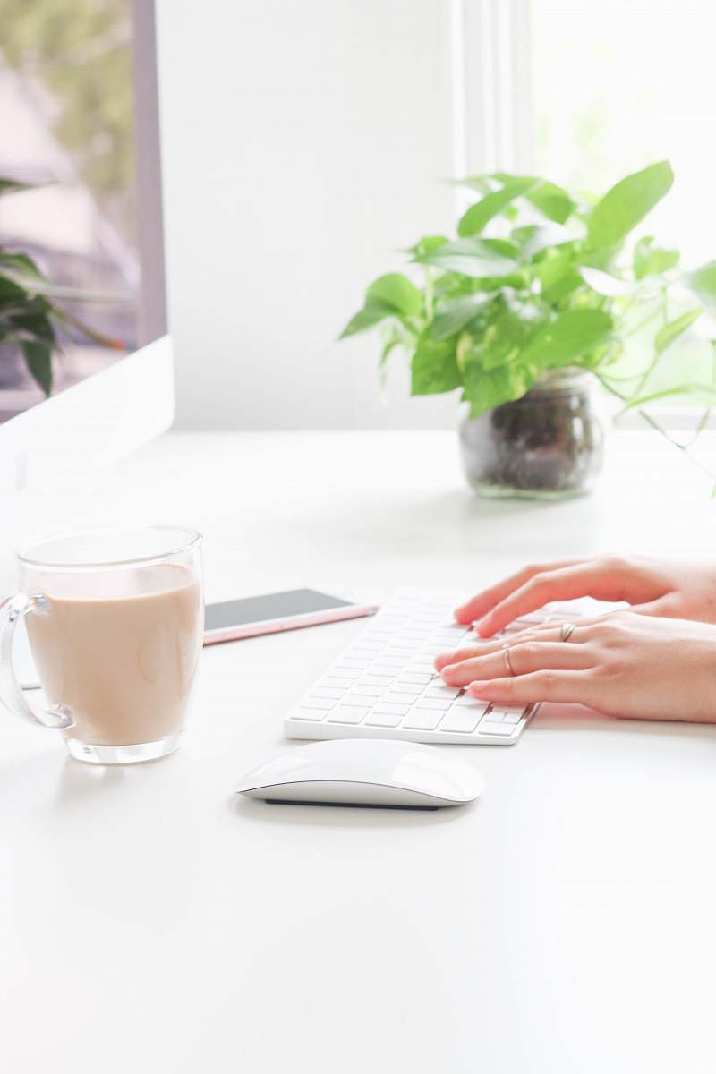 work person using Apple Wireless Keyboard near Apple Magic Mouse, mug, and rose gold iPhone 6s on table plant