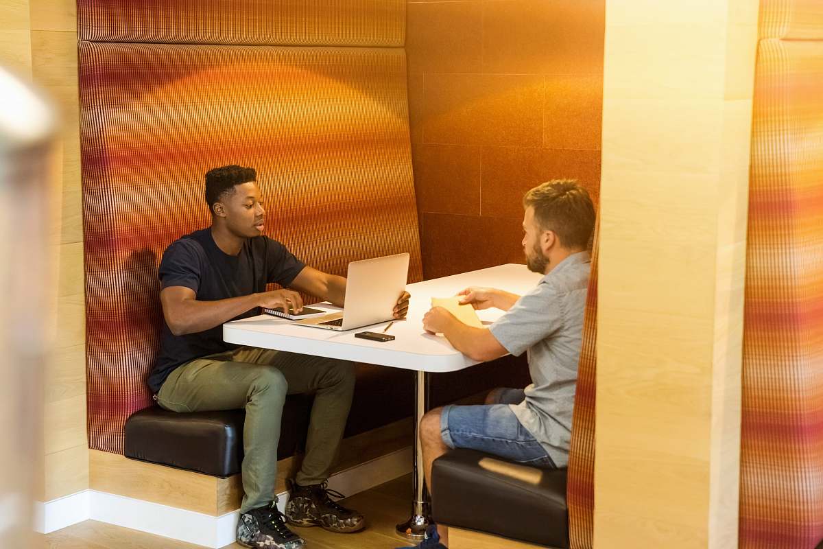 human man sitting on black leather bench holding gray laptop computer on top of white wooden table person
