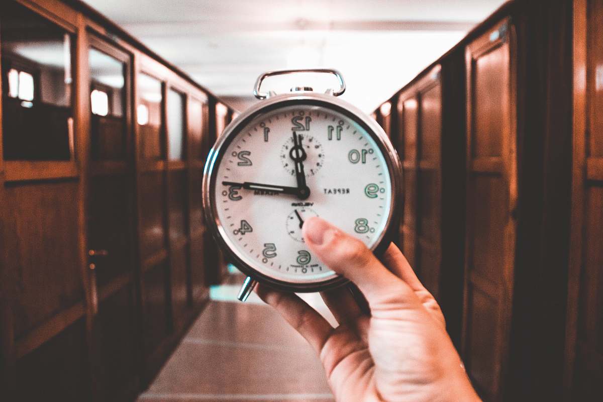 human person holding dual bell alarm clock reading at 12:14 o' clock person