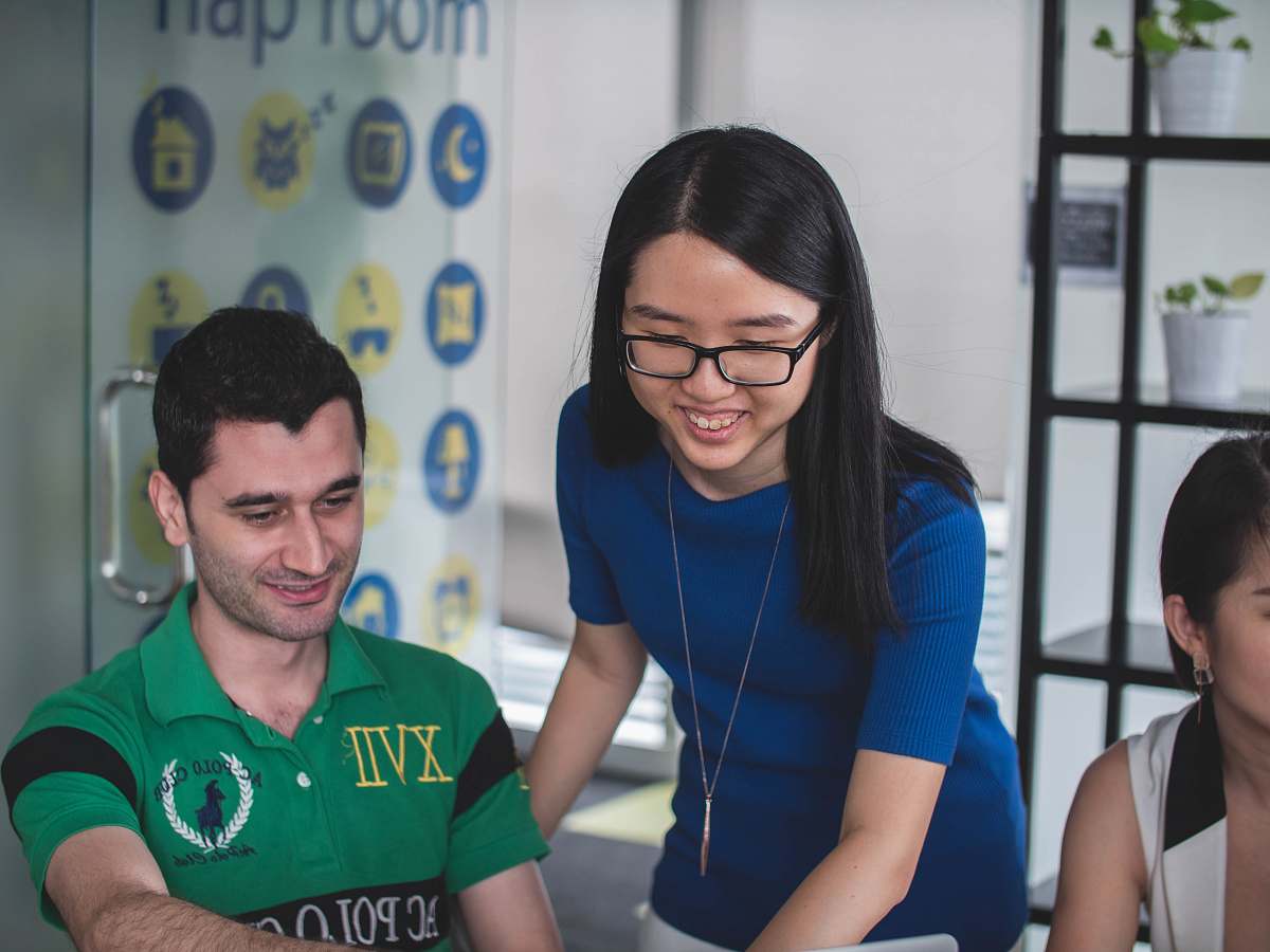 human smiling woman standing beside smiling man pointing MacBook person
