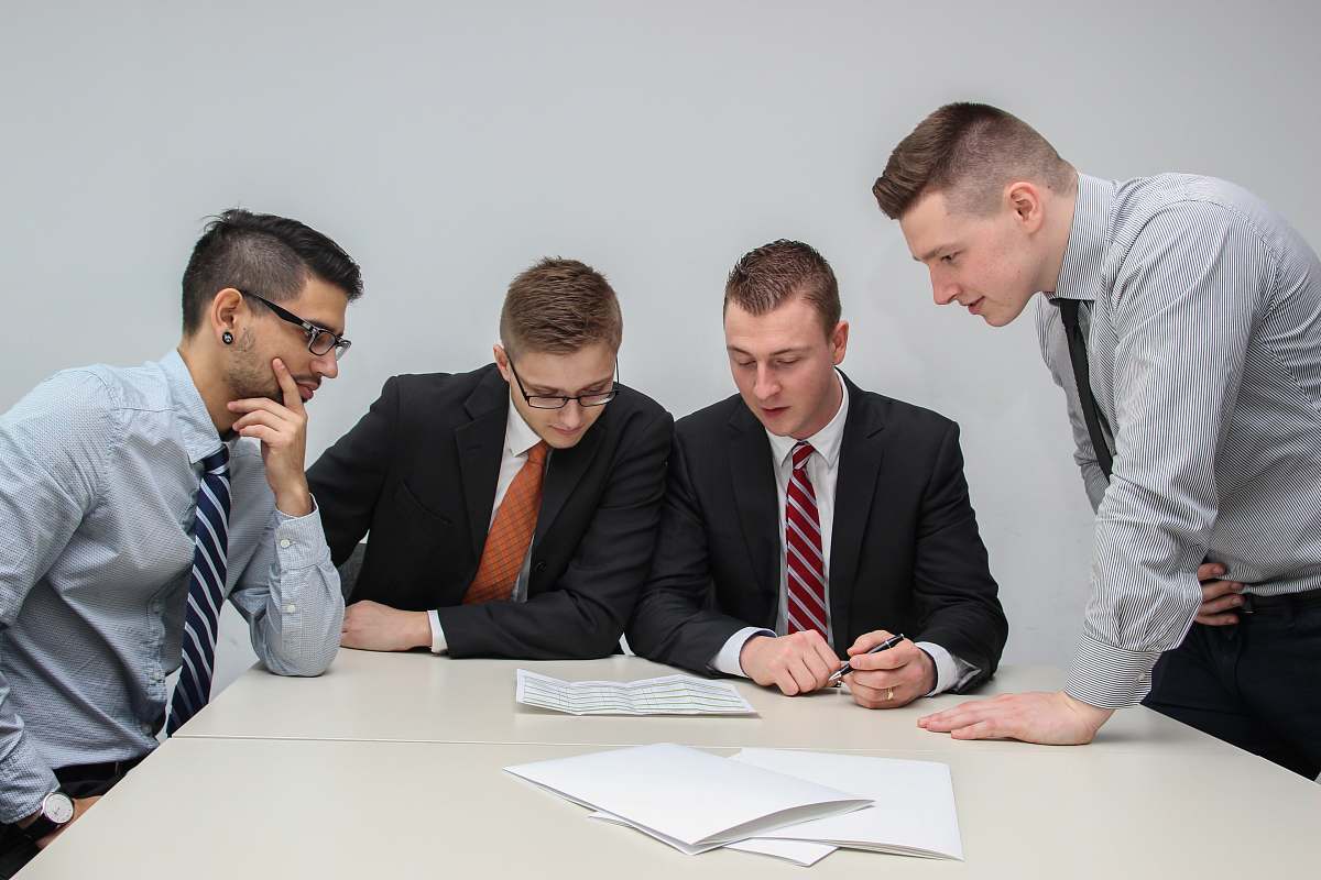 human four men looking to the paper on table sitting