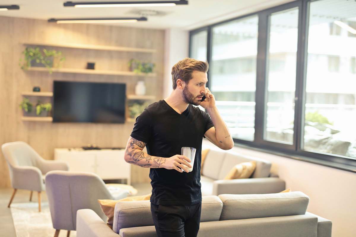 human man holding drinking glass while taking a call on phone couch