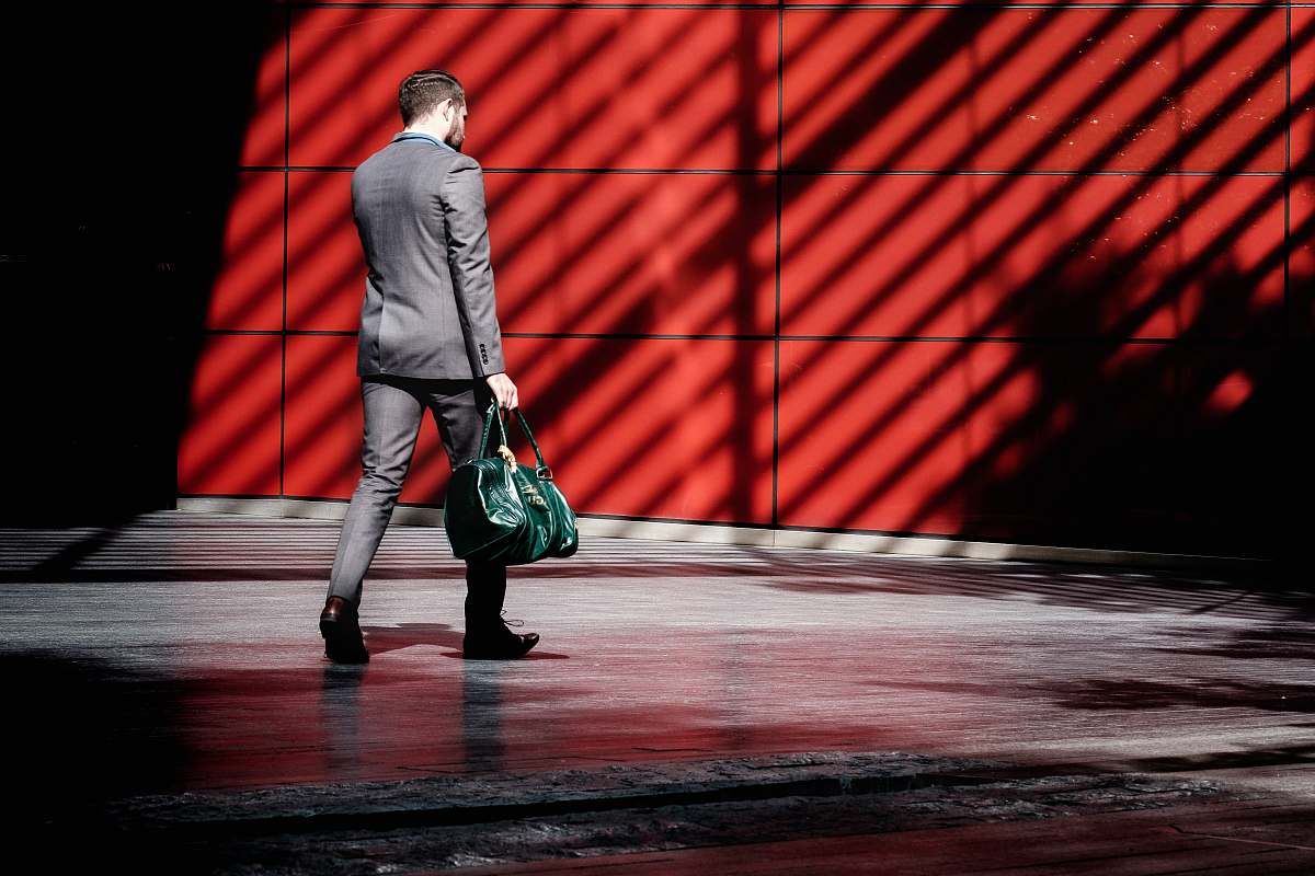 human man holding green duffel bag while walking near red building at daytime people