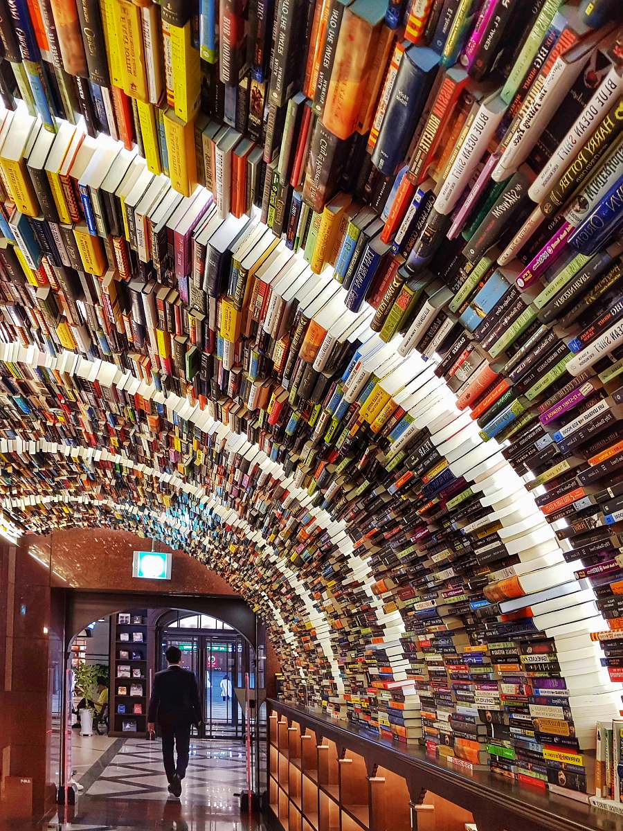 human man in black suit walking by the piled of books shop