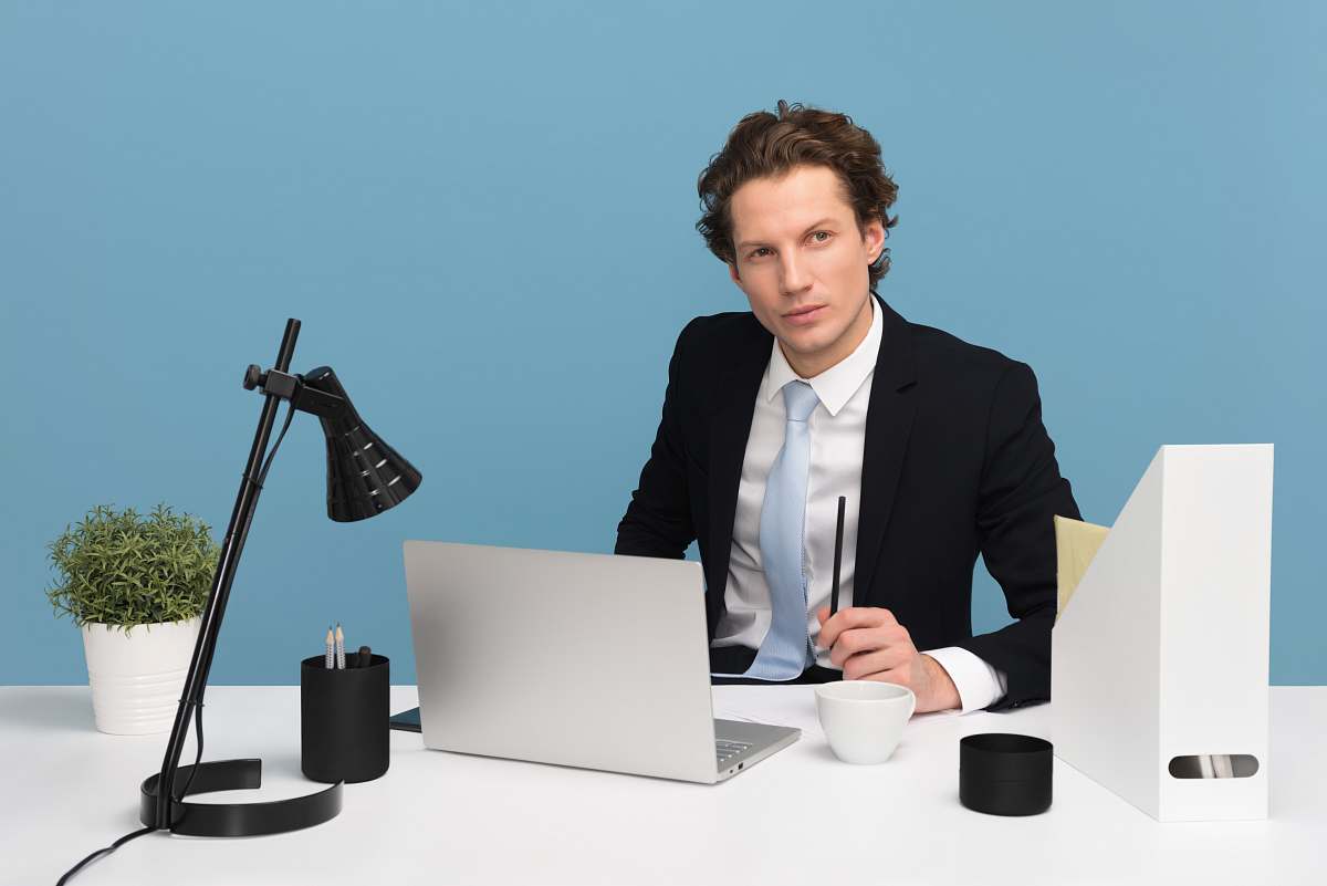 human man sitting on chair beside laptop computer and teacup sitting