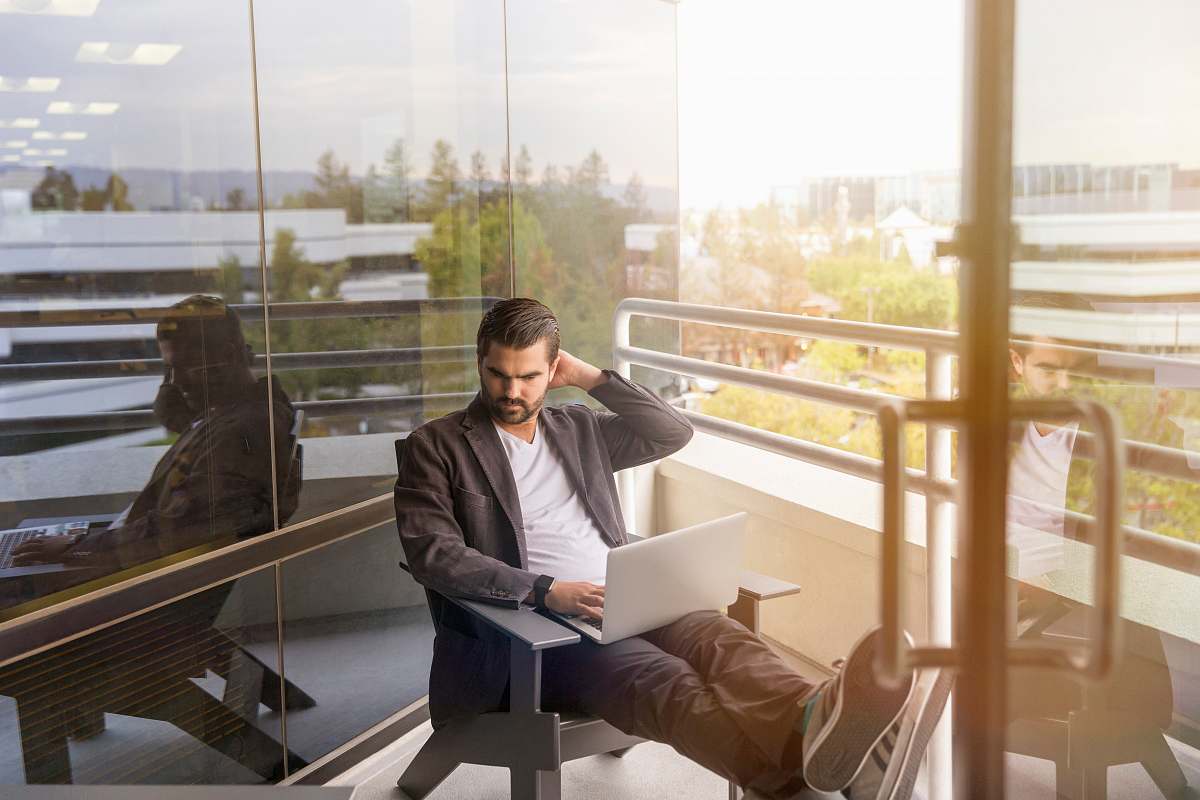 people man sitting on gray arm chair using silver laptop computer on building balcony at daytime human