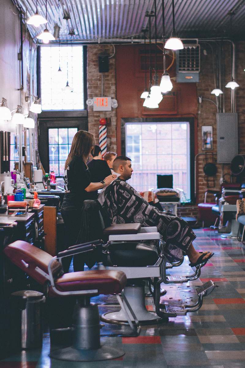 human man standing beside man sitting on barber chair people