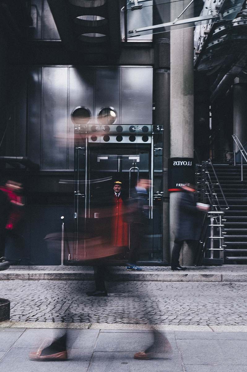 human man standing inside glass elevator in front of gray high-rise building during daytime people