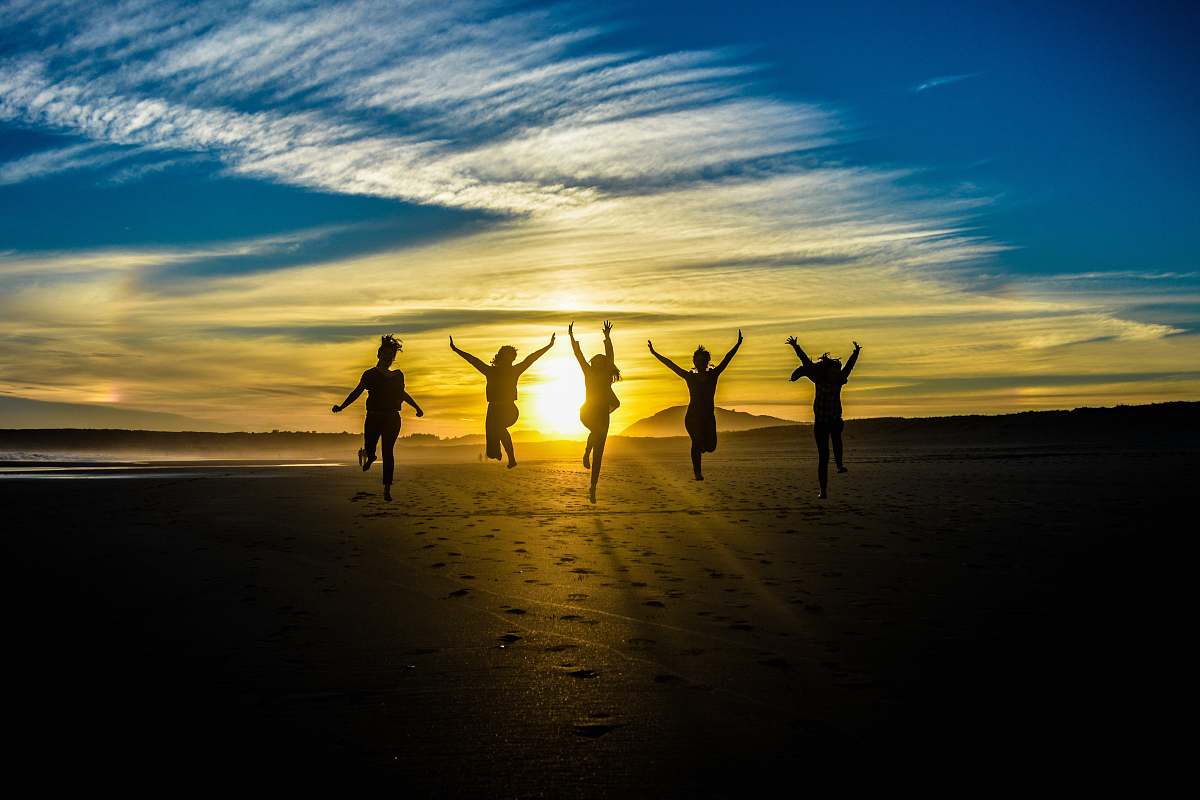 human people jumping on shore front of golden hour nature