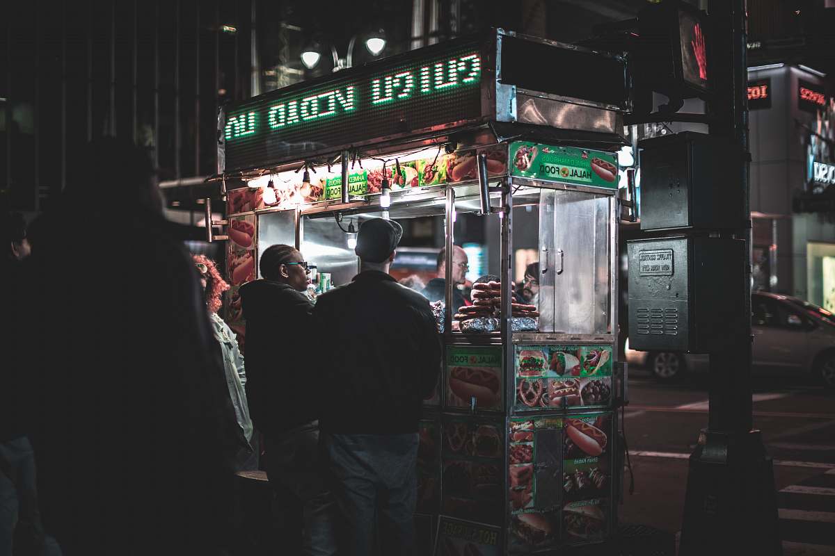 human two men standing in front of food cart besides black post during nighttime new york