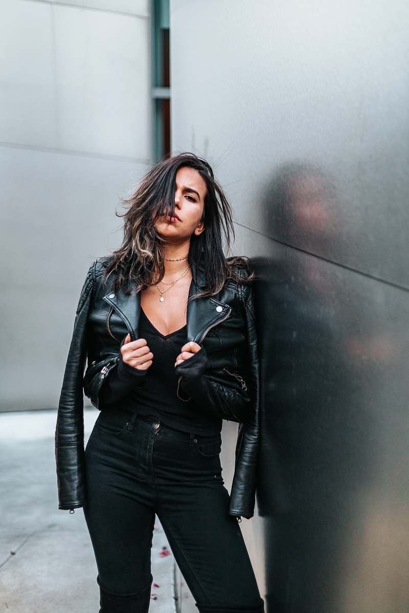 human woman touching her black leather jacket while standing near silver wall people