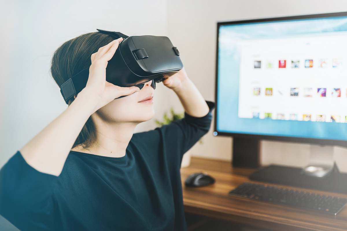 human woman using black VR headset beside computer people