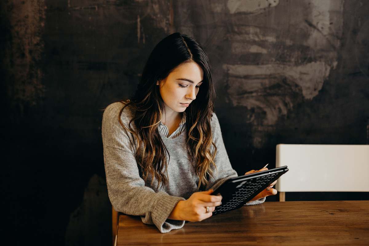 human woman wearing white dress shirt using holding black leather case on brown wooden table wood