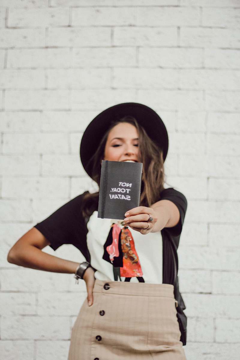 human woman with left arm akimbo standing and smiling while holding booklet apparel