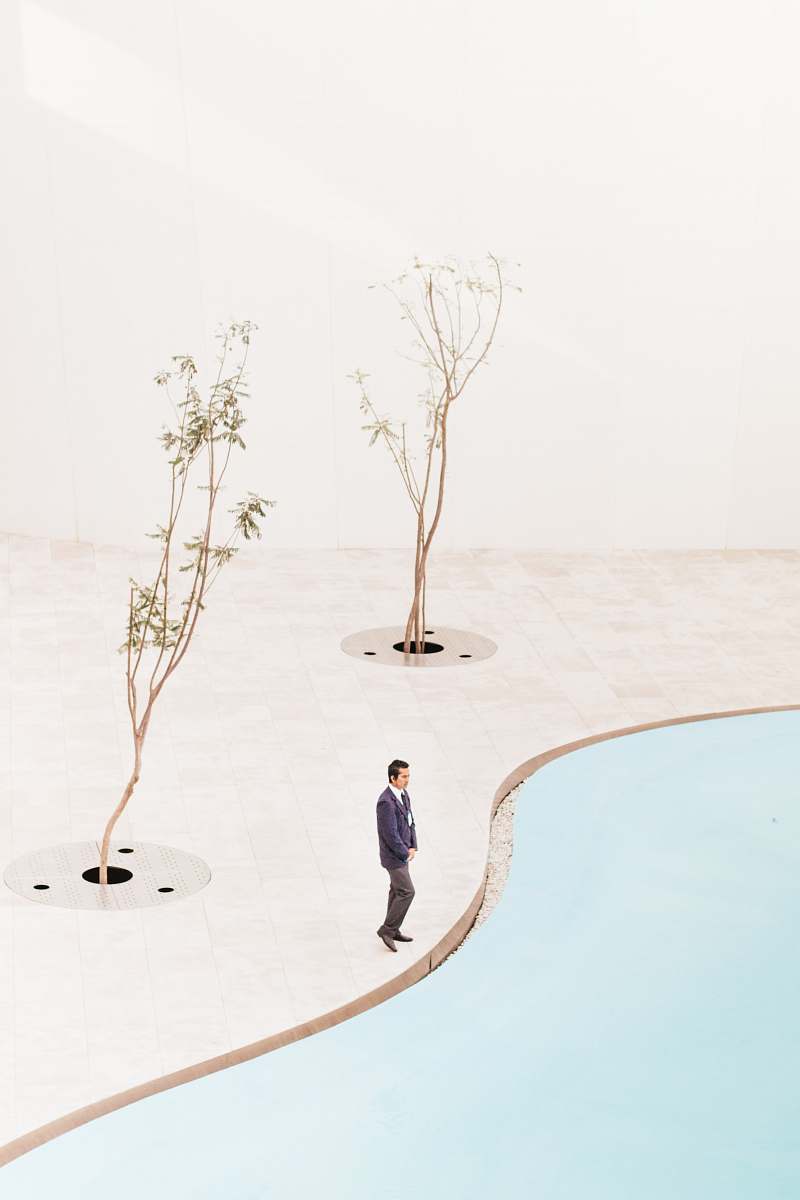 Capture the essence of creativity and relaxation with this striking image of an artist standing confidently near two lush trees by a serene poolside during the daytime. This vibrant scene perfectly embodies the harmony between nature and artistic expression, making it ideal for use in promotional materials, wellness blogs, or lifestyle magazines focused on art, leisure, and outdoor living.