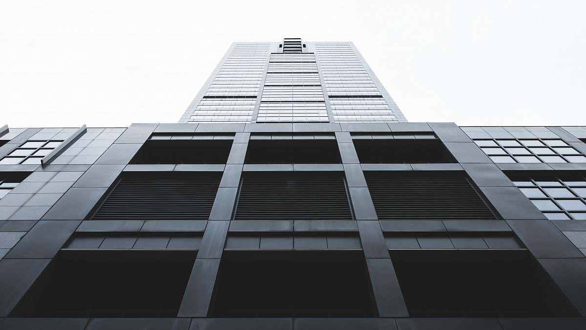 Experience the grandeur of modern architecture with this striking low angle photograph showcasing a tall high-rise building adorned with numerous windows against a vibrant sky backdrop. This image captures the essence of urban life and architectural brilliance, making it perfect for use in real estate marketing, architecture blogs, or business presentations that emphasize cityscapes and modern design.