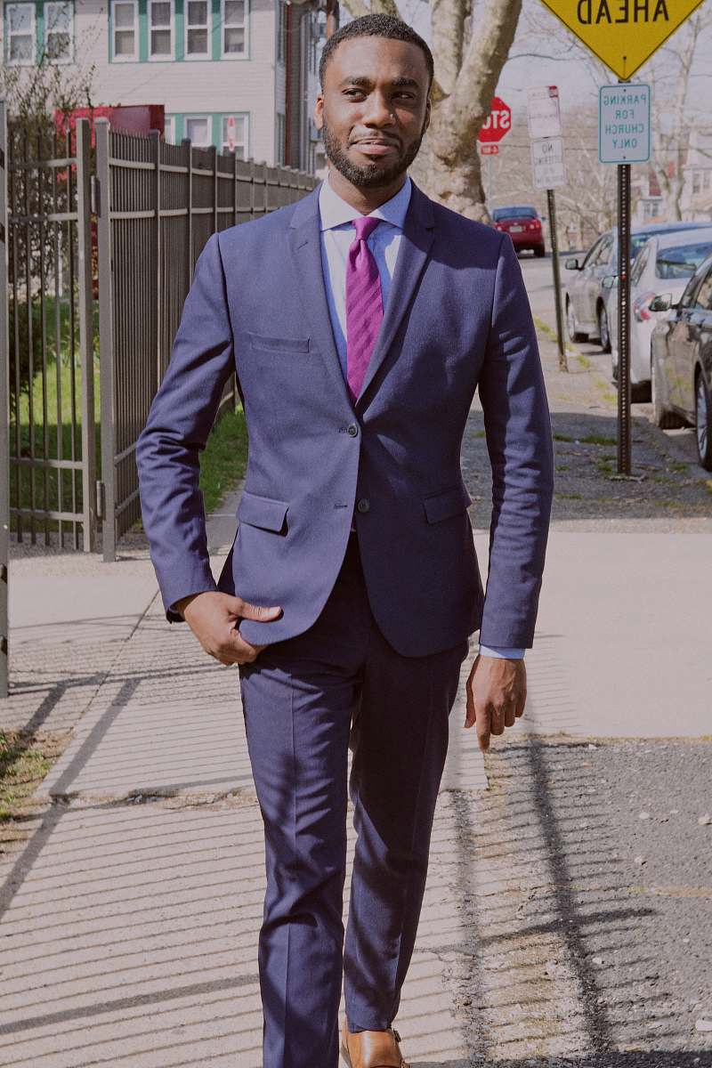 person man in blue suit walking on the sidewalk near metal fence and parked vehicle human