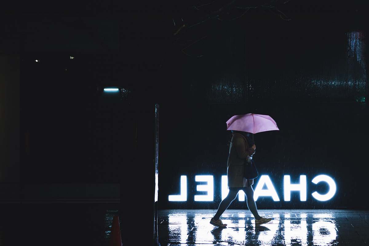 japan woman walking under umbrella passing by Chanel lighted signage canopy