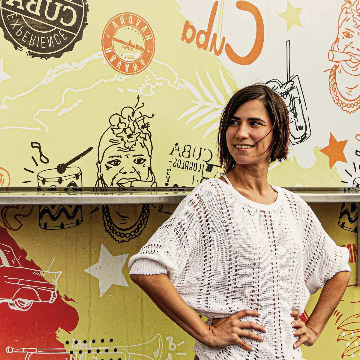 owner woman wearing white sweater near wall with art paint  smiling