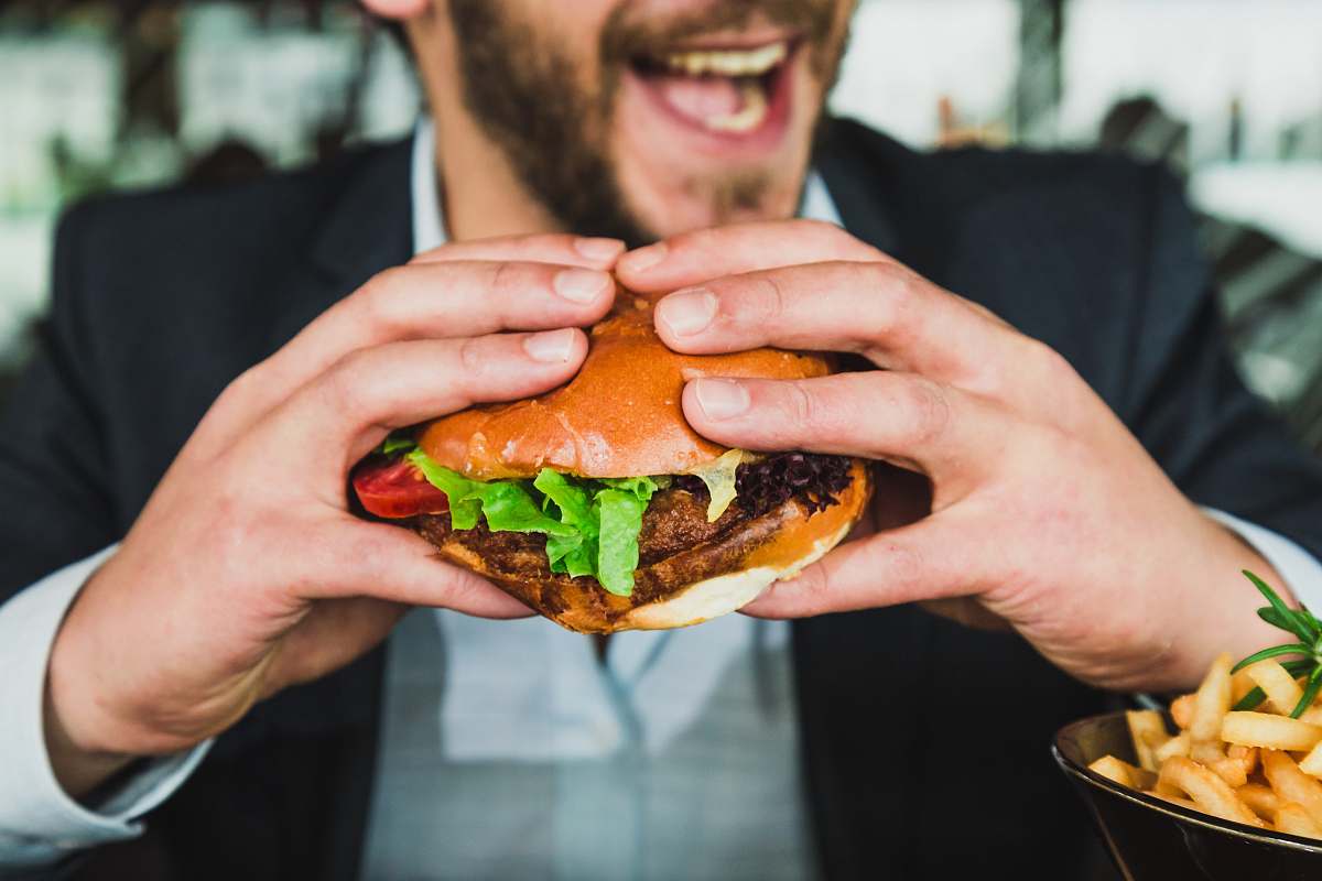 food person holding burger bun with vegetables and meat person