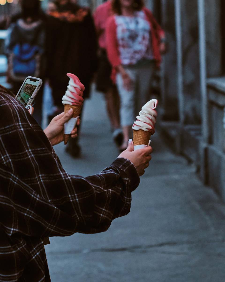 creme person standing while holding two ice cream in cone dessert